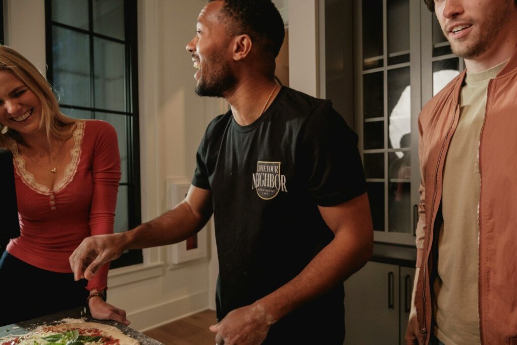 Man adding toppings to pizza with friends laughing