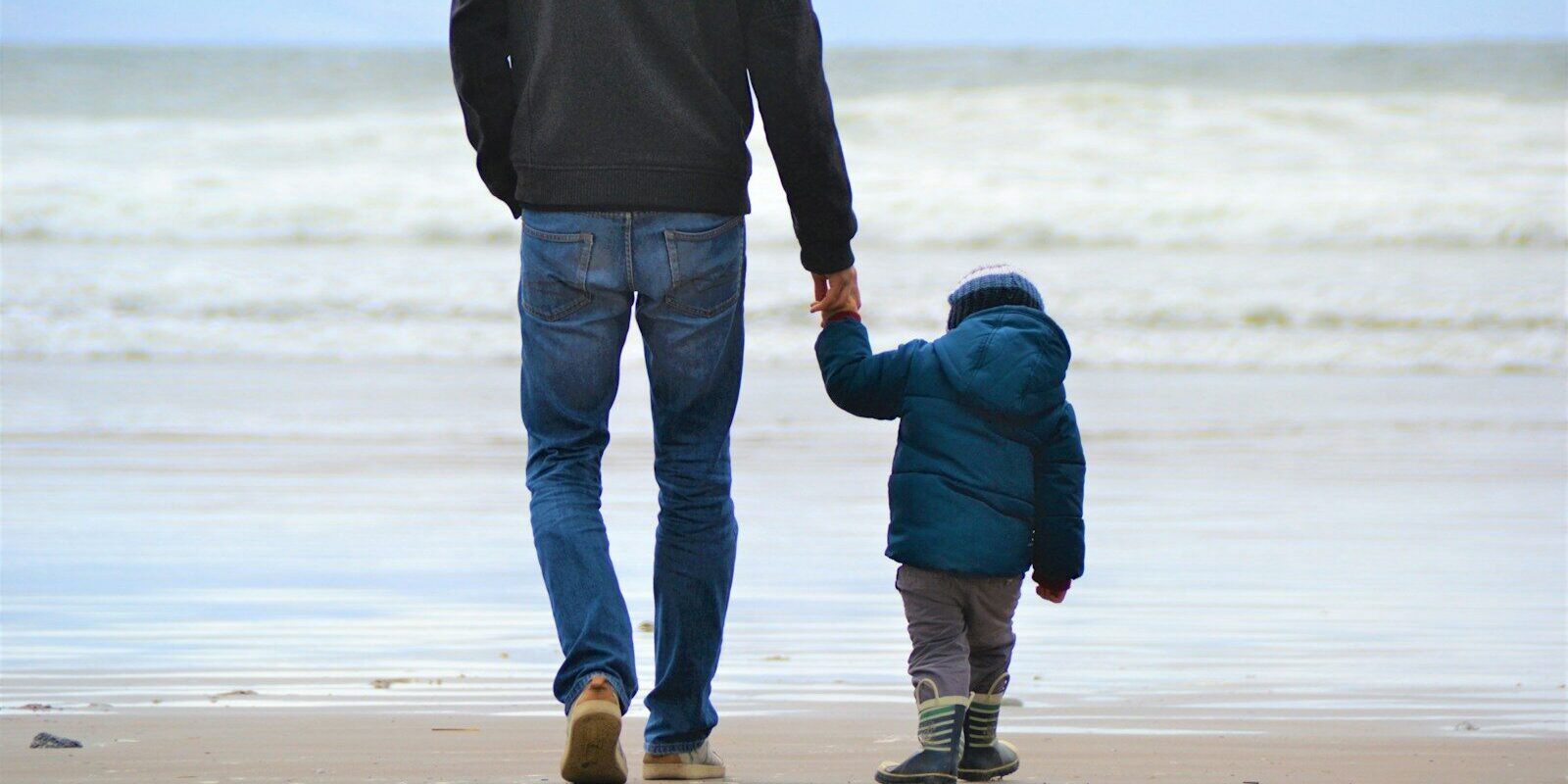 man and boy walking on seashore under blue sky